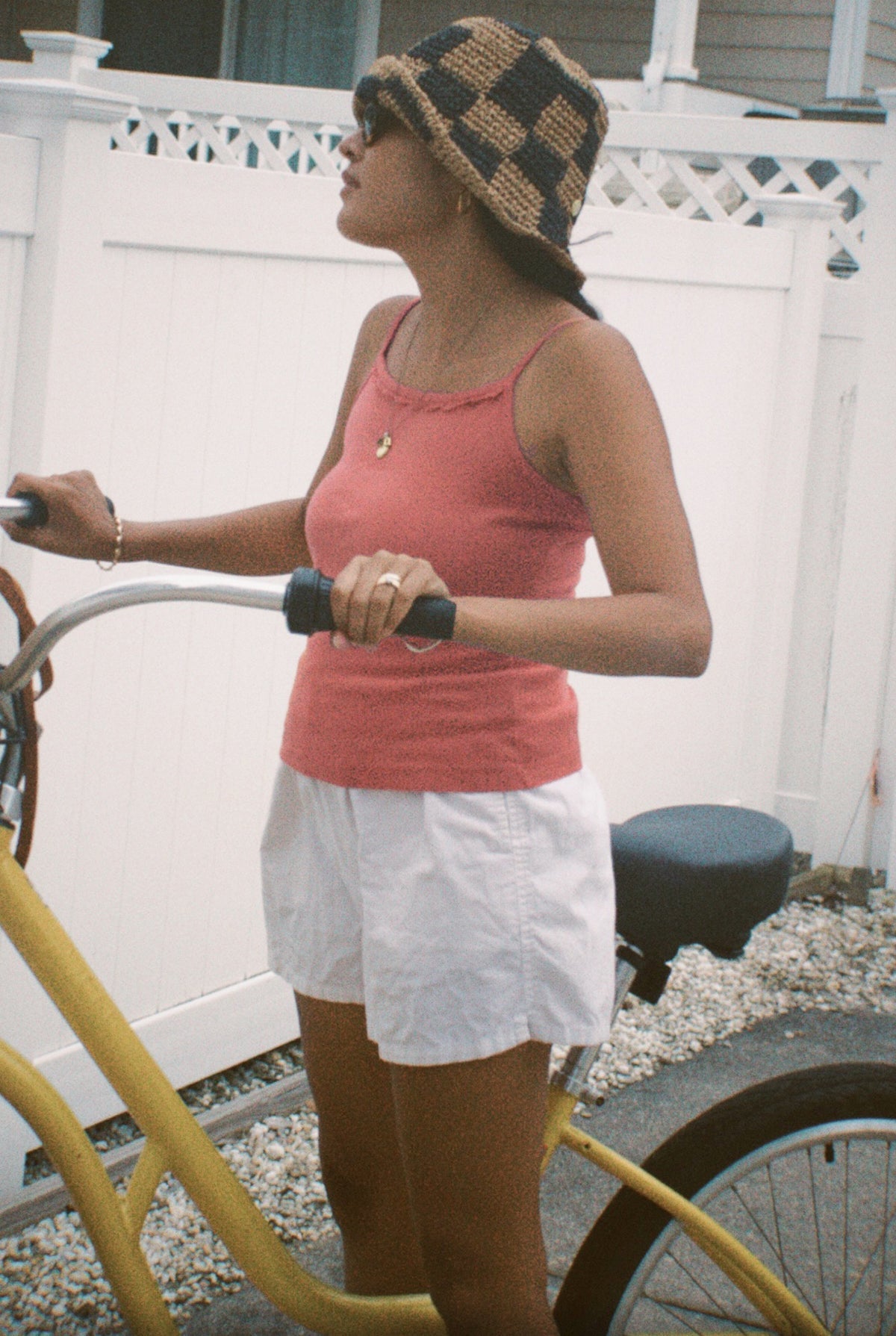 Rose -
Wearing LA RELAXED's Frill Camisole in pink, a person with a checkered bucket hat, sunglasses, and white shorts stands outdoors holding a yellow bike, with a white fence and house behind them.