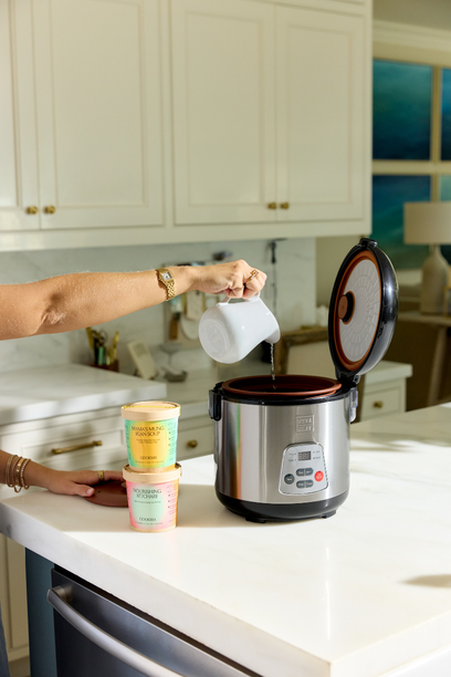 Close-up of an iced coffee or milk tea surface with frothy bubbles. A large, partially submerged ice cube with a slightly transparent and brownish appearance is visible on the left.