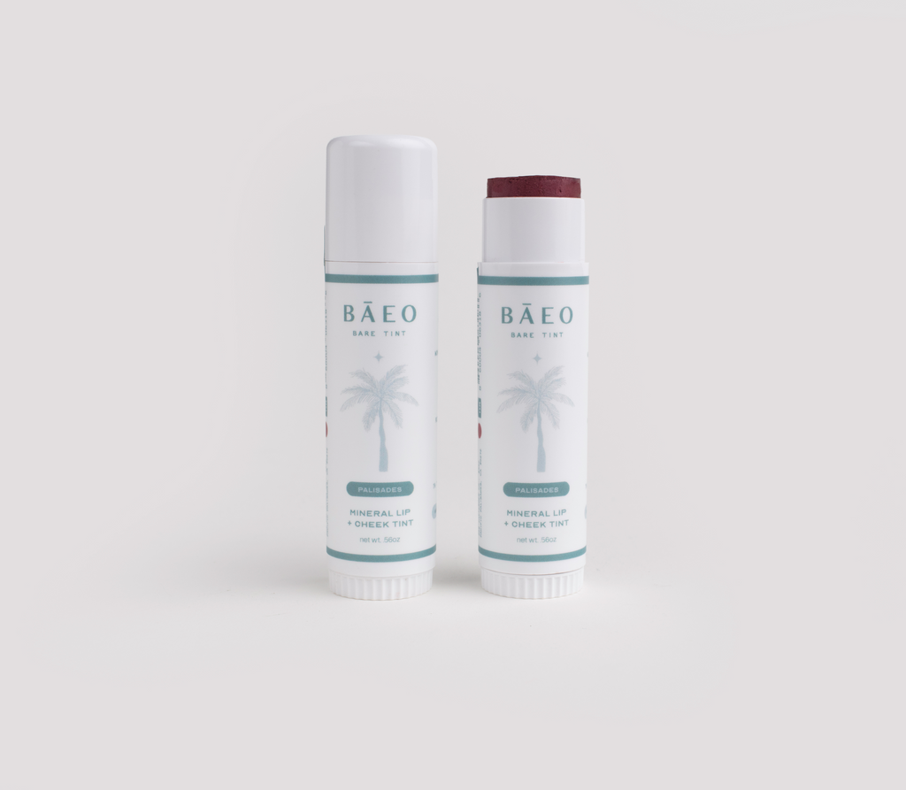 Two bāeo bare tint 'palisades' tubes, labeled "Mineral Lip + Cheek Tint" with a palm tree on the white label, stand side by side—one capped, one open to reveal a deep red hydrating tint for buildable color and a natural dewy finish.