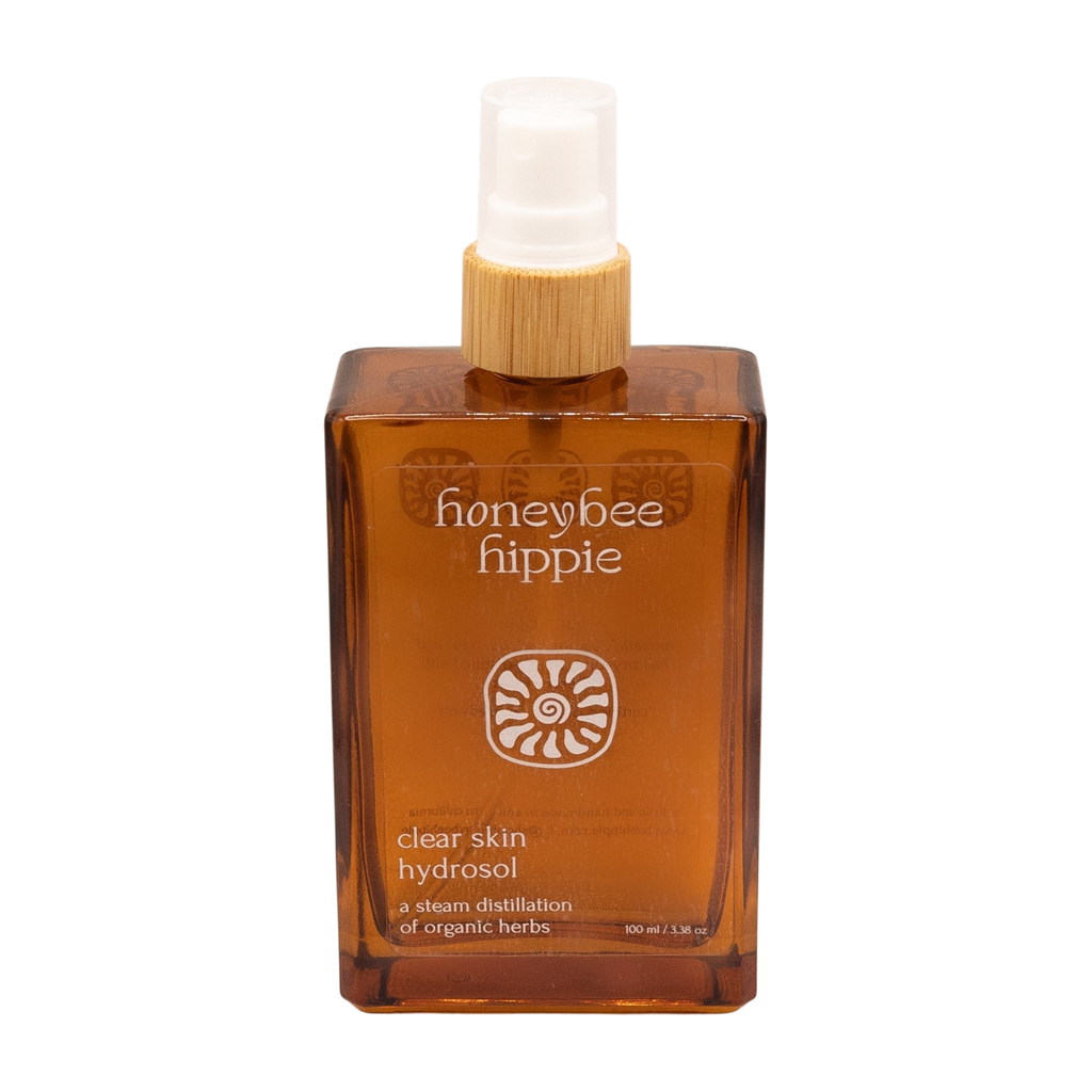 The Honeybee Hippie clear skin hydrosol comes in an amber spray bottle with a wooden cap and white nozzle, made from organic botanicals to complement green tea skincare routines.