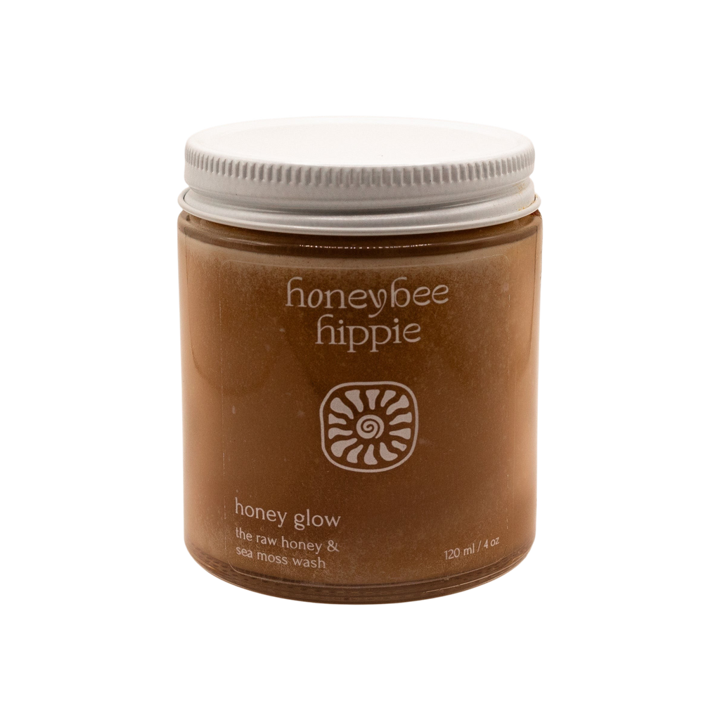A minimalist brown jar with a white lid, labeled "Honeybee Hippie" and "honey glow," contains raw honey and sea moss wash—a gentle, soap-free facial cleanser—displayed against a plain white background.