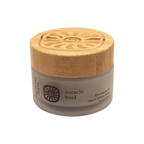 A small frosted glass jar with a wooden lid labeled "miracle mud" by Honeybee Hippie displays a spiral sun, offering skin comfort as a herbal balm enriched with bentonite clay for rescue and repair.