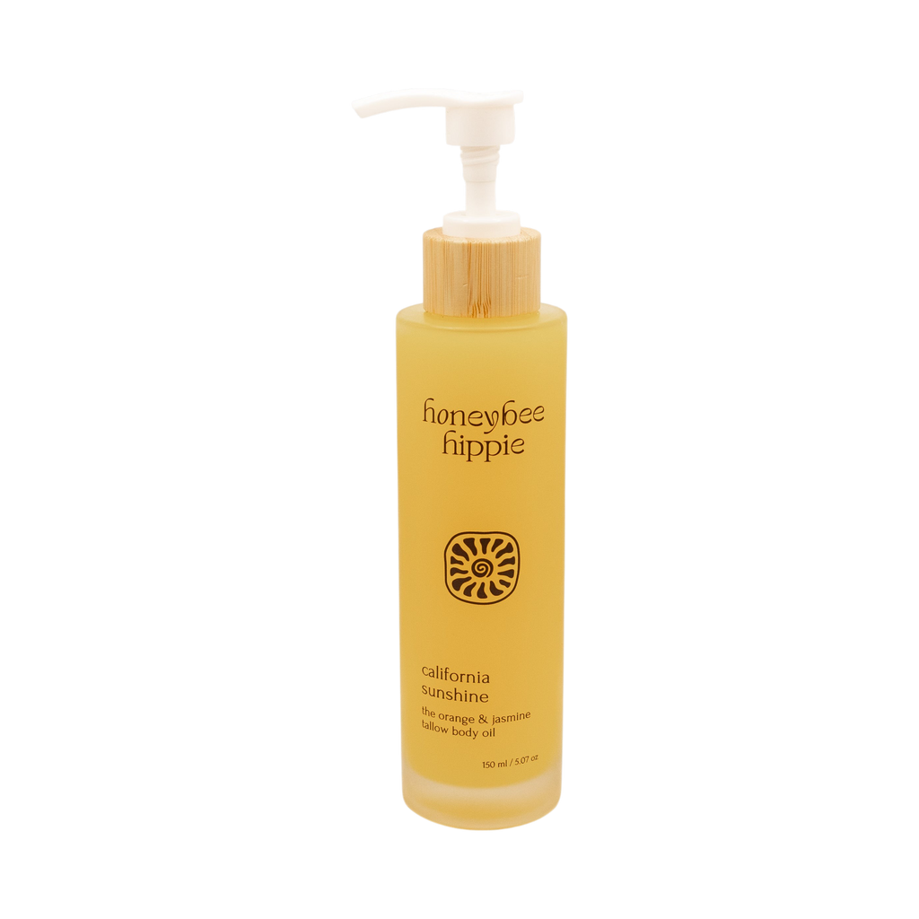 A 150 ml yellow bottle of Honeybee Hippie California Sunshine skin nourishing oil with a white pump, bamboo accent, and label featuring blue orange & jasmine, grass-fed suet tallow, and organic jojoba oil.