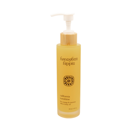A 150 ml yellow bottle of Honeybee Hippie California Sunshine skin nourishing oil with a white pump, bamboo accent, and label featuring blue orange & jasmine, grass-fed suet tallow, and organic jojoba oil.