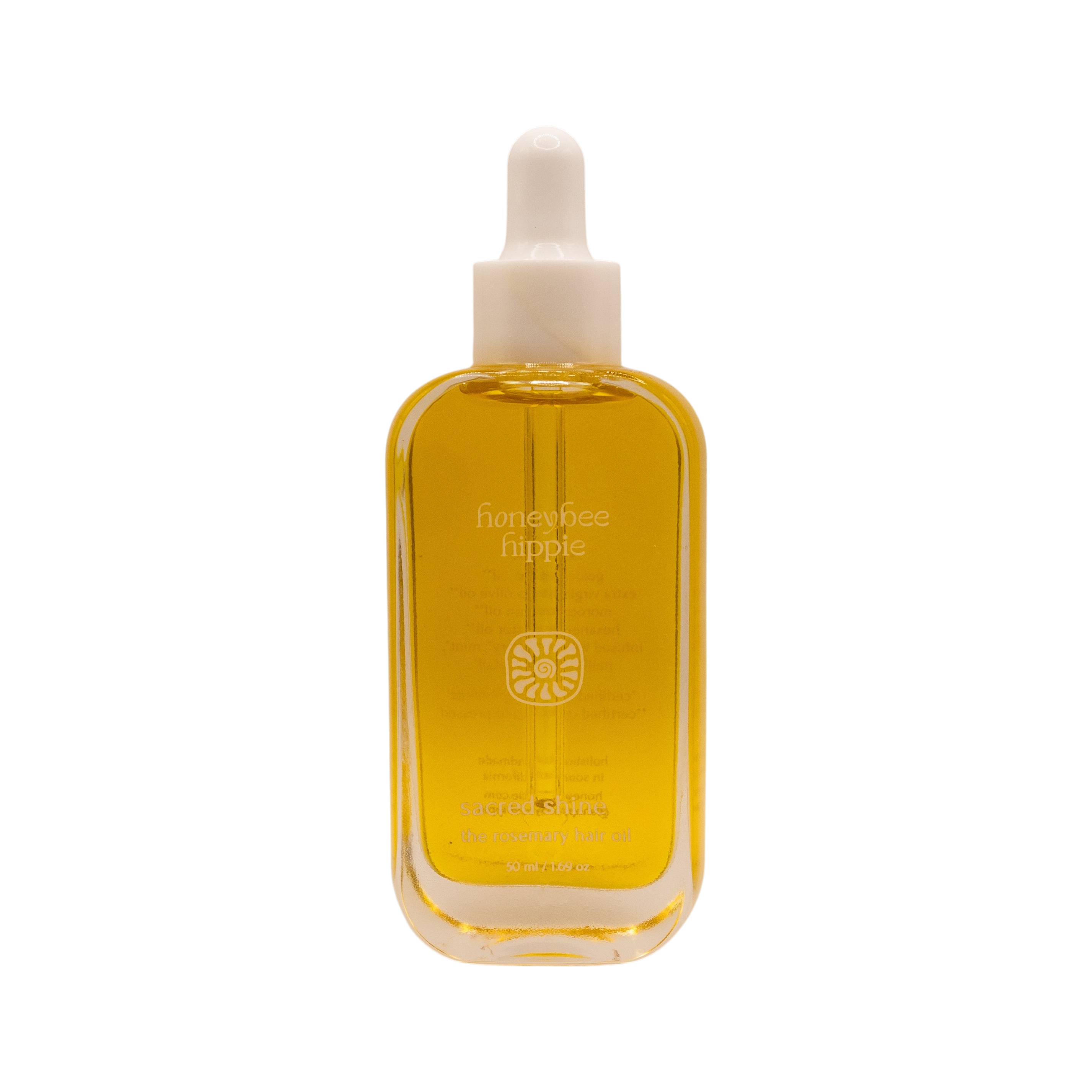 A clear glass bottle of golden yellow hair oil with a white dropper cap; the label reads "Honeybee Hippie" and "sacred shine hair oil" with additional text below.