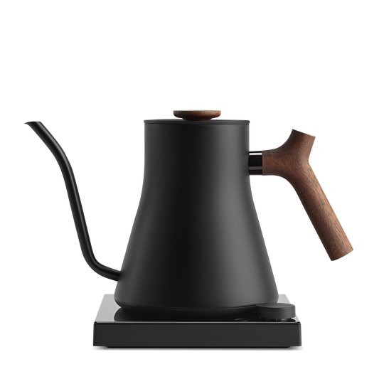 The Stagg EKG Pro Electric Kettle | Studio Edition by Fellow Wholesale is a sleek and modern appliance with a matte black finish. It boasts customizable brew settings and precision temperature control, paired with a curved spout for precise pouring. The kettle also features a wooden handle and lid knob, all elegantly sitting on its minimalist black base.