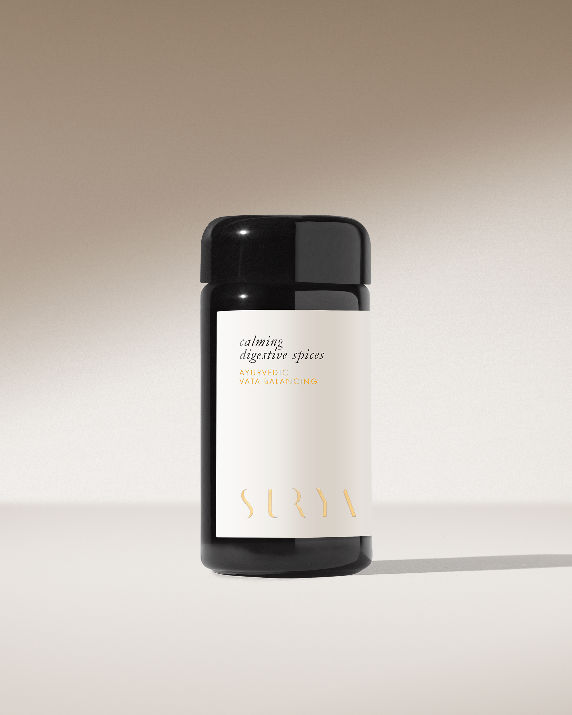 A black cylindrical jar labeled "Calming Digestive Spices" by Surya sits on a smooth surface against a beige gradient background—ideal as an Ayurvedic Vata-balancing spice blend for dahl or seasoning vegetables.