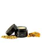 A small dark jar of Wild Mamas Baby- Wild Bison Tallow Balm (2 oz) with the lid resting nearby, surrounded by dried chamomile and calendula—gentle care for newborn skin on a white background.