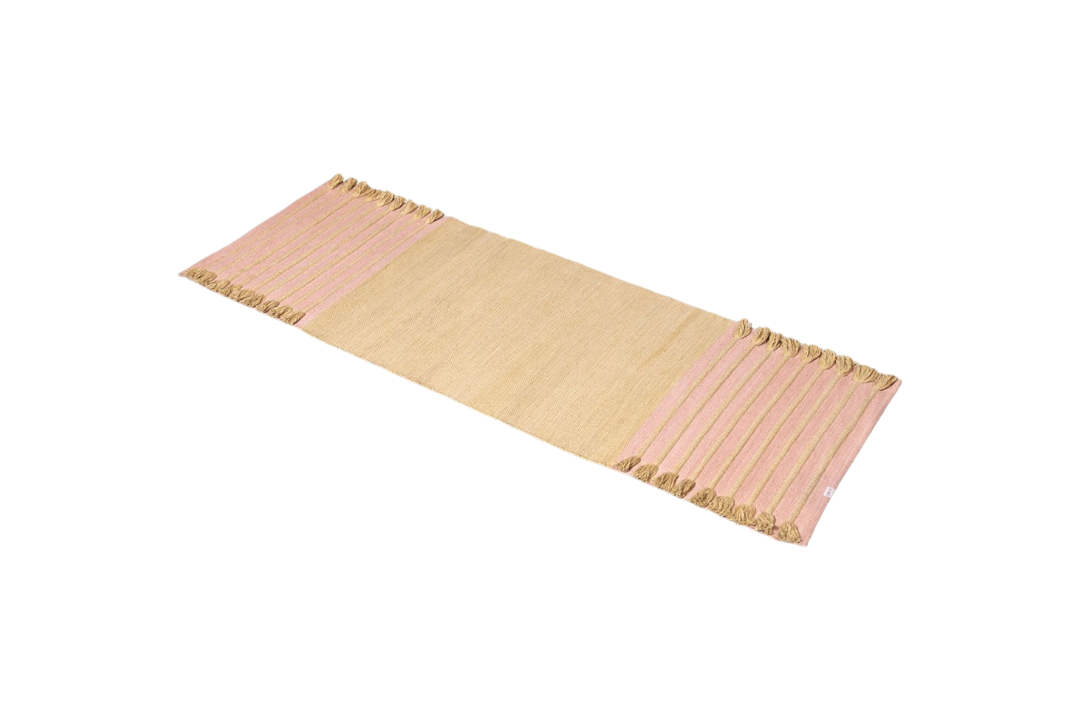 Harda and Madder Root Ayurvedic Yoga Mat by Bennd Yoga, featuring rectangular beige design with pink-striped edges and tasseled ends, crafted from organic cotton, set against a white background.