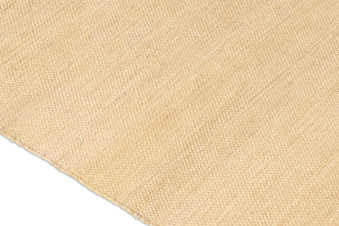 Close-up view of a beige woven textile with a textured surface, resembling the Harda and Madder Root Ayurvedic Yoga Mat from Bennd Yoga. Made from natural fibers, the fabric displays a gentle variation in tone across the material.