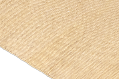 Close-up view of a beige woven textile with a textured surface, resembling the Harda and Madder Root Ayurvedic Yoga Mat from Bennd Yoga. Made from natural fibers, the fabric displays a gentle variation in tone across the material.