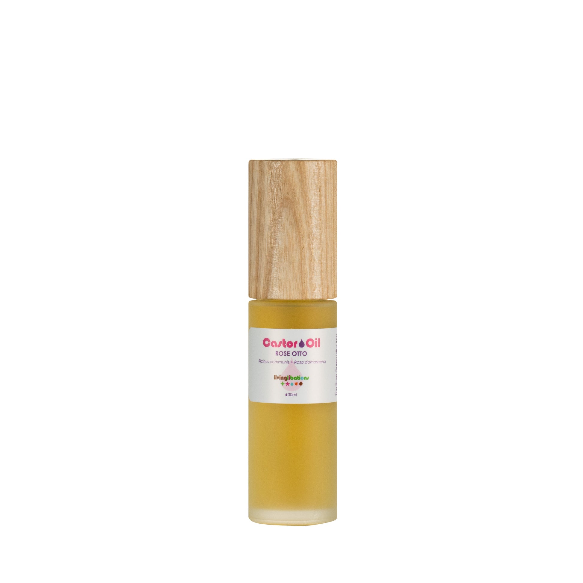 A bottle of Living Libations Castor Oil + Rose Otto, capped with wood and filled with a golden liquid. The label features "Castor Oil + Rose Otto" above a colorful logo.
