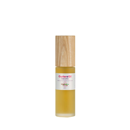 A bottle of Living Libations Castor Oil + Rose Otto, capped with wood and filled with a golden liquid. The label features "Castor Oil + Rose Otto" above a colorful logo.