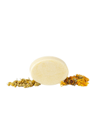 The Wild Mamas Chamomile + Calendula (Baby) Wild Bison Tallow Soap, a round pale yellow bar, stands upright on a white background between two small piles of dried chamomile and calendula flowers.