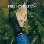 A bottle of Summer Solace Tallow Emanations Profound Face Oil rests on green leaves with water droplets. Above, white text reads "DEEP HYDRATION." A white flower is near the center. The oil features tallow, emu oil, champa & ginger lily.