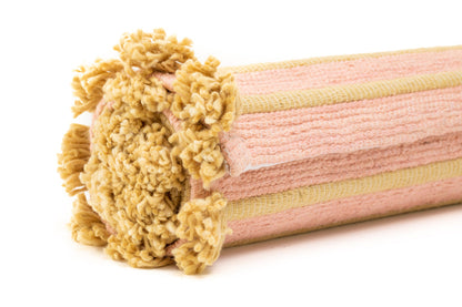 Close-up of the Harda and Madder Root Ayurvedic Yoga Mat by Bennd Yoga, showcasing its cylindrical shape with a pink and beige fabric design made from organic cotton. The end highlights soft, curly beige fibers crafted to block air drafts from door gaps.