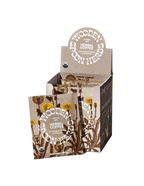 A product display box of WOODEN SPOON HERBS Herbal Coffee, highlighting a caffeine-free blend with multiple individual packets. The packaging features illustrations of dandelion and other plants in a natural earthy color scheme, with text indicating USDA organic certification and the inclusion of adaptogenic mushrooms.