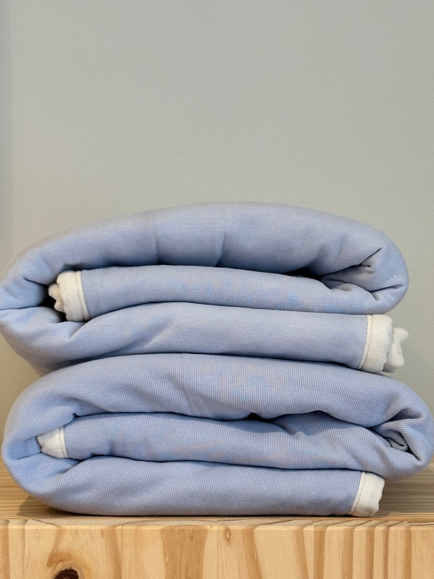 An indigo BABY BLANKET by cabane childrenswear is neatly folded, featuring a hand-quilted design with white edges, resting on a wooden surface against a plain light gray background.