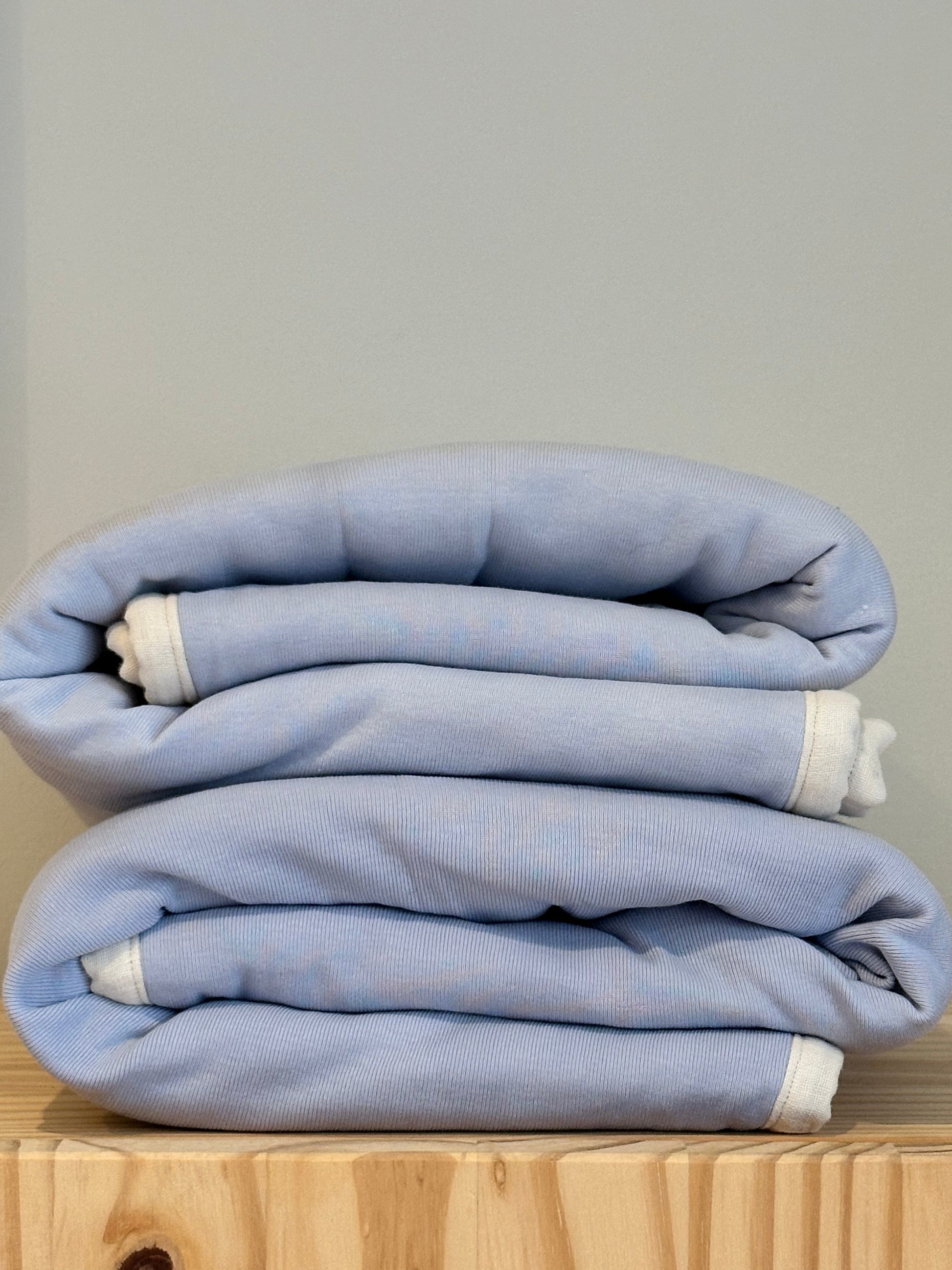 An indigo BABY BLANKET by cabane childrenswear is neatly folded, featuring a hand-quilted design with white edges, resting on a wooden surface against a plain light gray background.