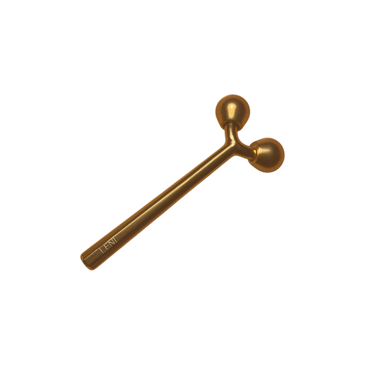 The LENI THE FACE TOOL, a gold-toned metal facial roller with a handle and twin round ends, is perfect for lymphatic massage and better skincare absorption. It is shown against a plain white background.