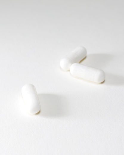 Three DOSAGE Mother-of-Pearl capsules are scattered on a pristine white surface. The image boasts a minimalistic and bright aesthetic, emphasizing the simplicity and uniformity of the capsules. Faint shadows add depth to the otherwise plain background.