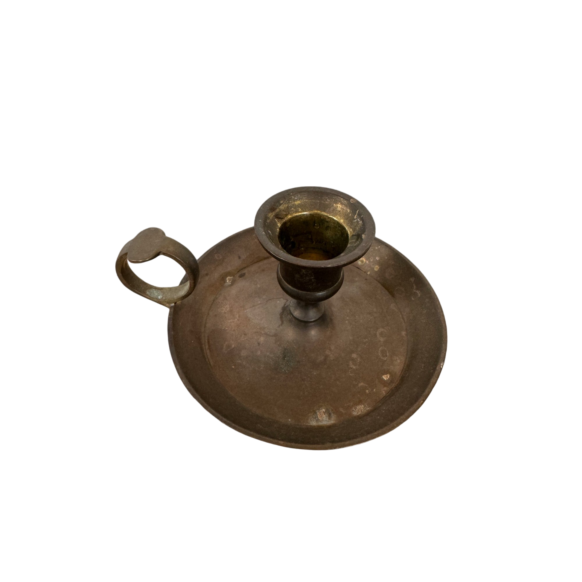 The Brass Candle Holder II by Shoppe Maison features a vintage design with a circular base and a finger loop handle on one side. The tarnished metal reflects its age and wear, adding to its antique charm. A drip tray encircles the empty candle socket, and the black background accentuates the timeless elegance of this piece.