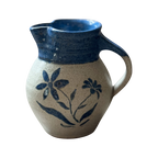 The Shoppe Maison Stoneware Creamer features a handmade salt-glazed ceramic style with a blue-glazed rim and handle, decorated with hand-painted blue flowers on a beige background.