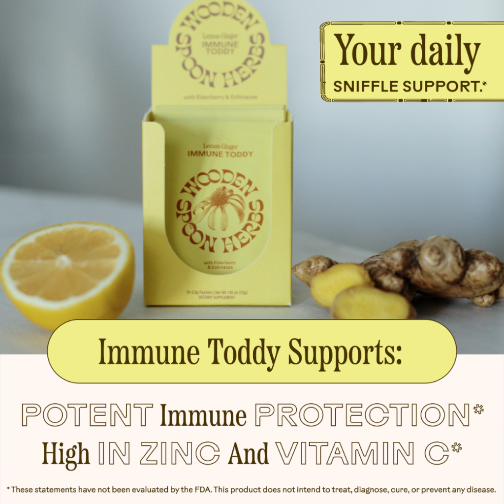 A box of WOODEN SPOON HERBS Lemon-Ginger Immune Toddy sits on a surface beside lemon and ginger. Text highlights immune support with elderberry, high vitamin C, and daily sniffle support. FDA disclaimer is shown.