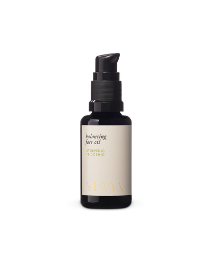 A dark amber bottle with a black pump dispenser features the "Balancing Face Oil" label along with "Ayurvedic Tridoshic." The white label, adorned with gold and black text, also highlights its inclusion of botanical retinol. The brand name "Surya" is elegantly printed in gold at the bottom.