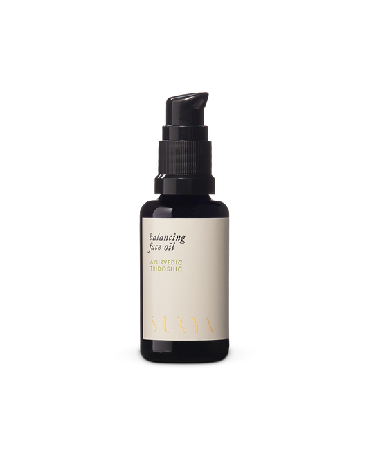 A dark amber bottle with a black pump dispenser features the "Balancing Face Oil" label along with "Ayurvedic Tridoshic." The white label, adorned with gold and black text, also highlights its inclusion of botanical retinol. The brand name "Surya" is elegantly printed in gold at the bottom.
