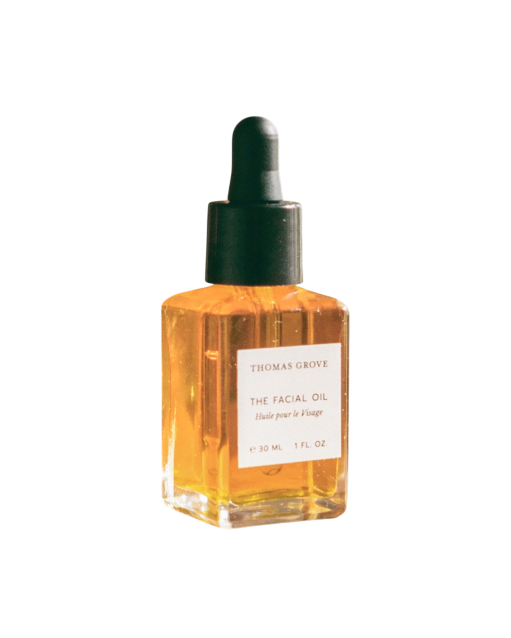 A small glass bottle of THOMAS GROVE SKIN THE FACIAL OIL with a black dropper cap, filled with golden-yellow liquid. The label shows ounces and milliliters, highlighting Bulgarian rose otto and rosehip seed oil.