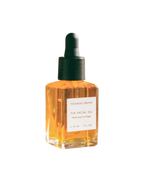 A small glass bottle of THOMAS GROVE SKIN THE FACIAL OIL with a black dropper cap, filled with golden-yellow liquid. The label shows ounces and milliliters, highlighting Bulgarian rose otto and rosehip seed oil.