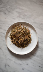 A white plate on a marble surface holds PLANTWALK’s RIVERBANK | Lymphatic Clarity Herbal Infusion, a blend of dried, shredded herbs commonly used for lymphatic system support and herbal lymphatic drainage.