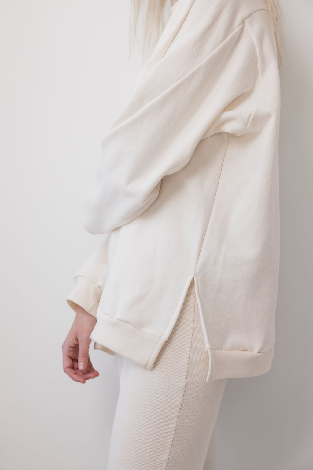 A person stands sideways against a plain white background, partially out of frame, wearing the Wol Hide Big Sweatshirt : Natural with its signature shoulder gusset and matching pants.