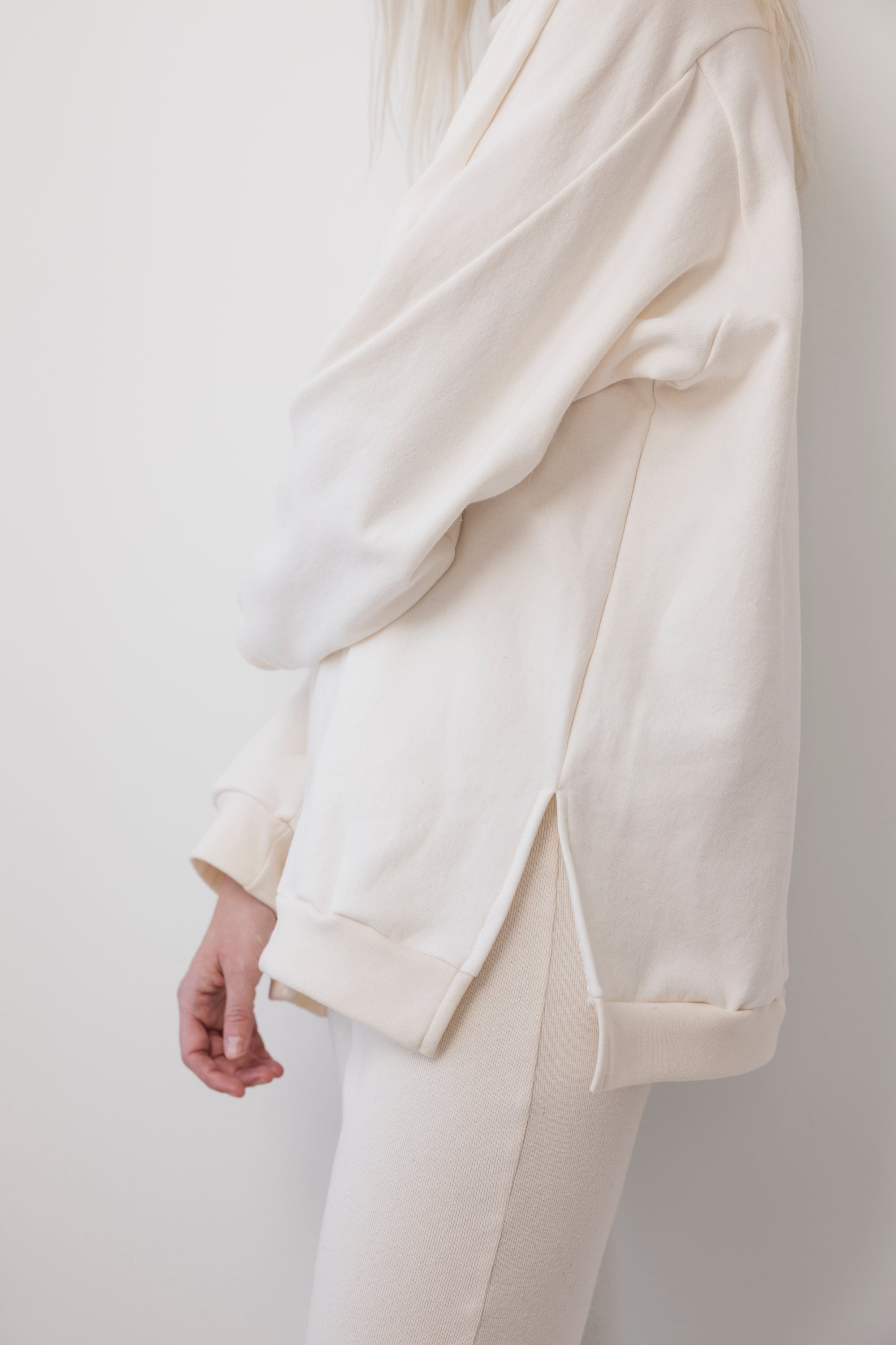 A person stands sideways against a plain white background, partially out of frame, wearing the Wol Hide Big Sweatshirt : Natural with its signature shoulder gusset and matching pants.