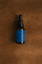 A small amber glass dropper bottle labeled "Emanations Profound Face Oil" by Summer Solace Tallow with a blue label sits on a brown textured surface—ideal for storing this deeply nourishing tallow, emu oil, and floral blend.