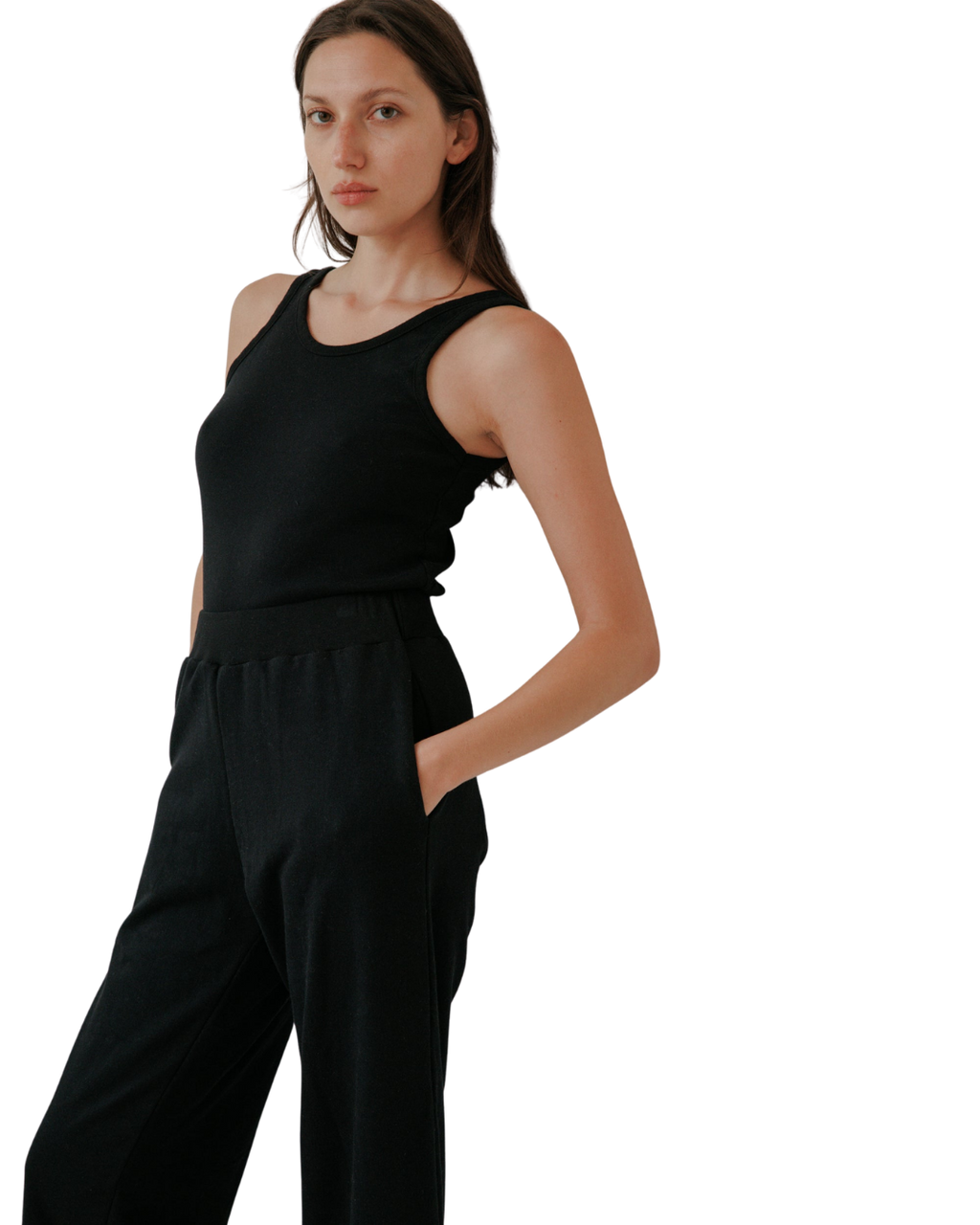 A woman with long brown hair wears the Wol Hide Scoop Back Rib Tank in black with matching pants, standing with one hand in her pocket against a light background, highlighting the effortless style of sustainable fashion.