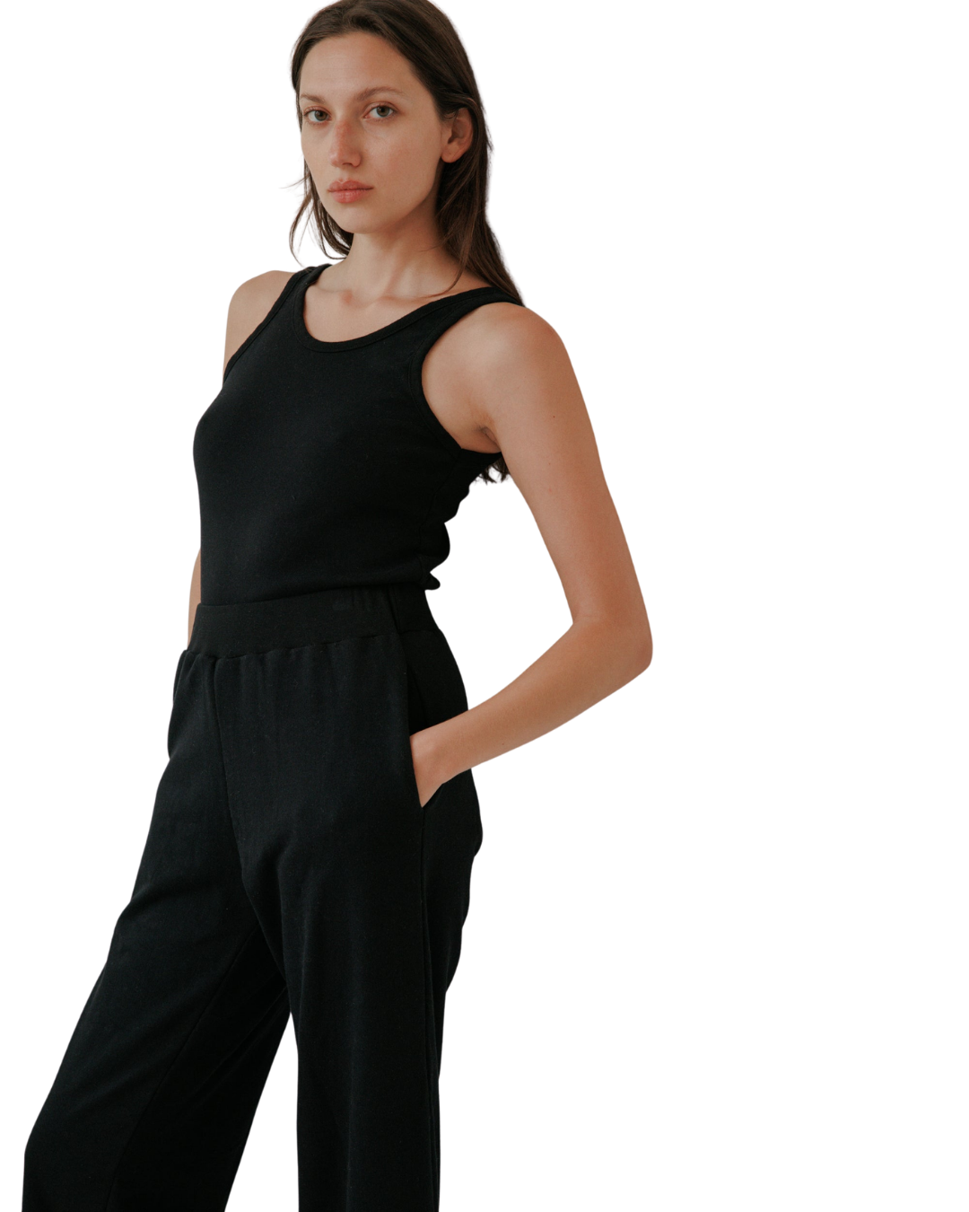 A woman with long brown hair wears the Wol Hide Scoop Back Rib Tank in black with matching pants, standing with one hand in her pocket against a light background, highlighting the effortless style of sustainable fashion.