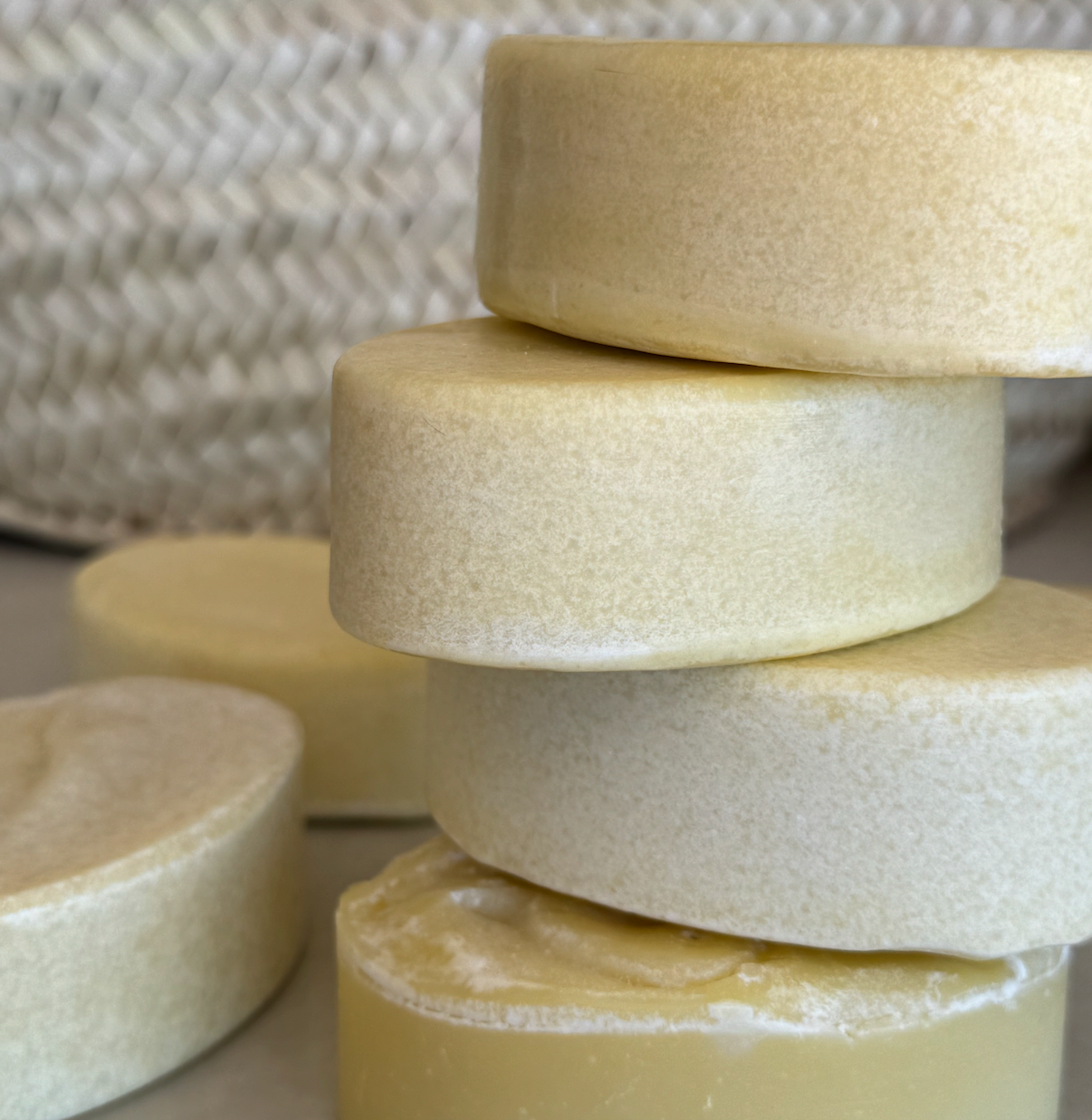 A close-up of several round Chamomile + Calendula (Baby) Wild Bison Tallow Soap bars by Wild Mamas, stacked in a small pile with a woven basket blurred in the background.