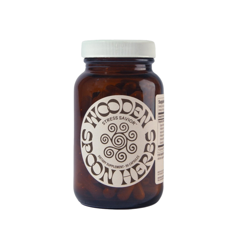 A brown glass jar with a white lid labeled "WOODEN SPOON HERBS Stress Savior" contains 90 adaptogen capsules for stress management, featuring a decorative circular design on the label.