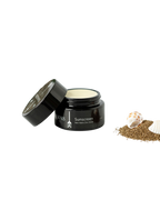 A black jar of Wild Mamas Sunscreen- Wild Bison Tallow Balm with the lid off sits beside brown sand and seashells on a white background. The label highlights broad-spectrum sun protection.