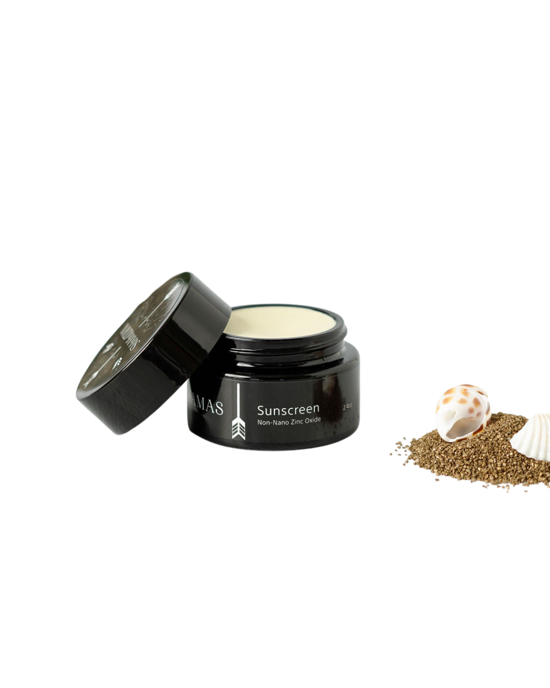 A black jar of Wild Mamas Sunscreen- Wild Bison Tallow Balm with the lid off sits beside brown sand and seashells on a white background. The label highlights broad-spectrum sun protection.