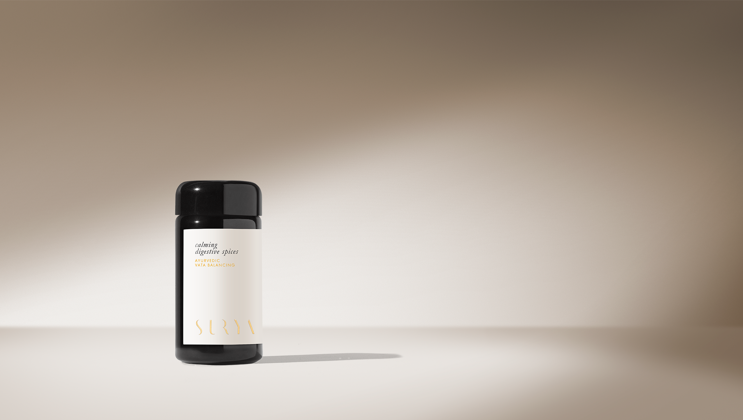 A single black bottle with a beige label reading "Calming Digestive Spices" and "Surya" stands on a smooth surface under a spotlight, casting a shadow. The scene evokes spice blend aromas reminiscent of cooking dahl on a soft beige gradient.