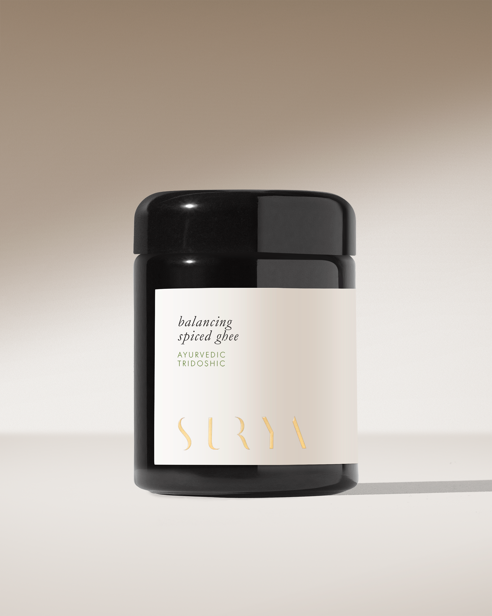 A black jar with a beige label reading "Spiced Ghee – Surya" sits on a neutral background, featuring organic ghee perfect for Ayurvedic cooking, enhanced with balancing spices.
