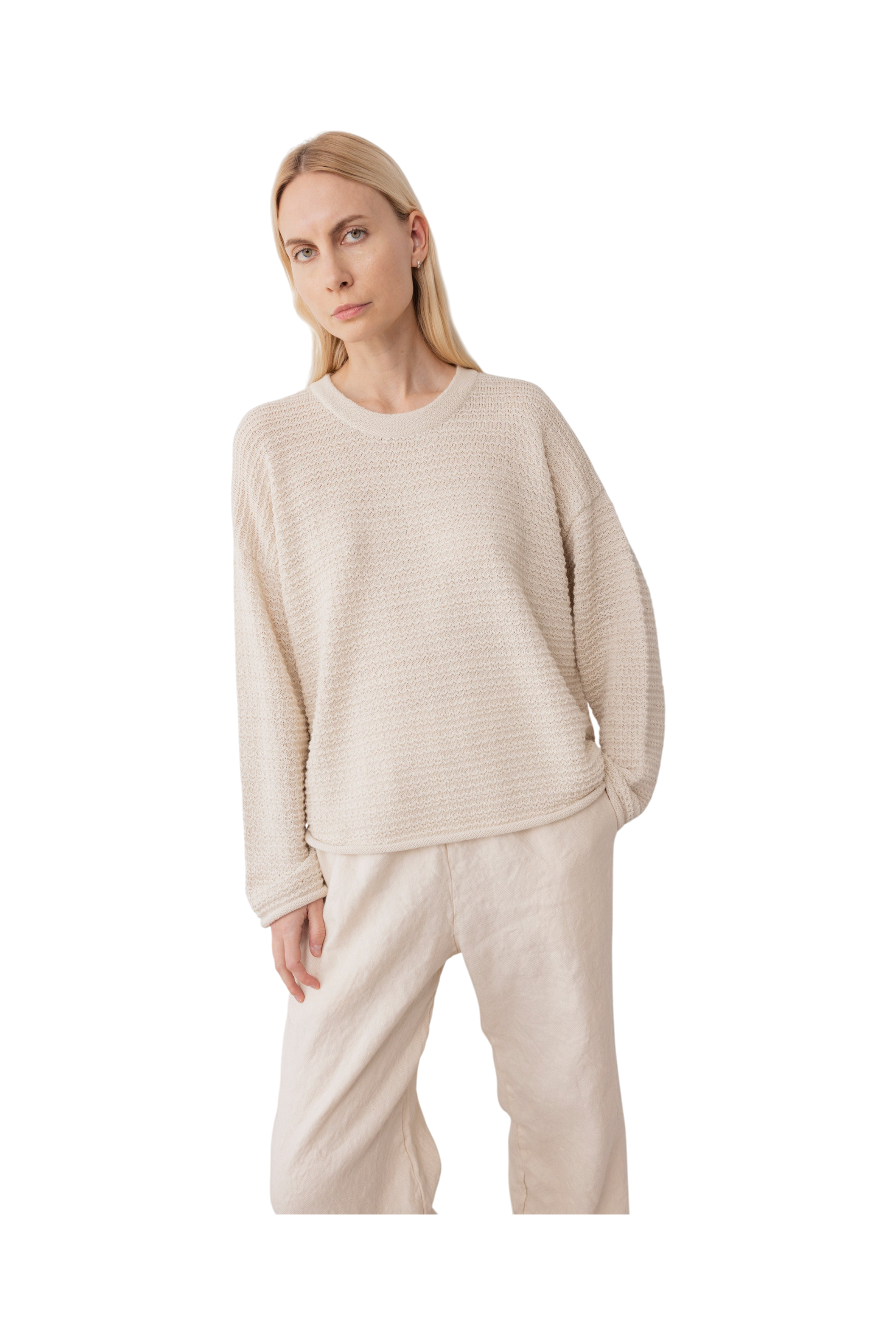 A woman with long blonde hair wears the Wol Hide Thermal Sweater in Natural and wide-leg beige pants, standing against a plain white background and capturing the spirit of slow fashion.