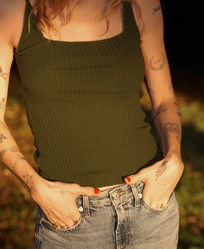 Wearing the LA Relaxed Pointelle Square Cami in green and blue jeans, a person with tattooed arms stands outdoors with hands in pockets as sunlight highlights their skin and clothing.
