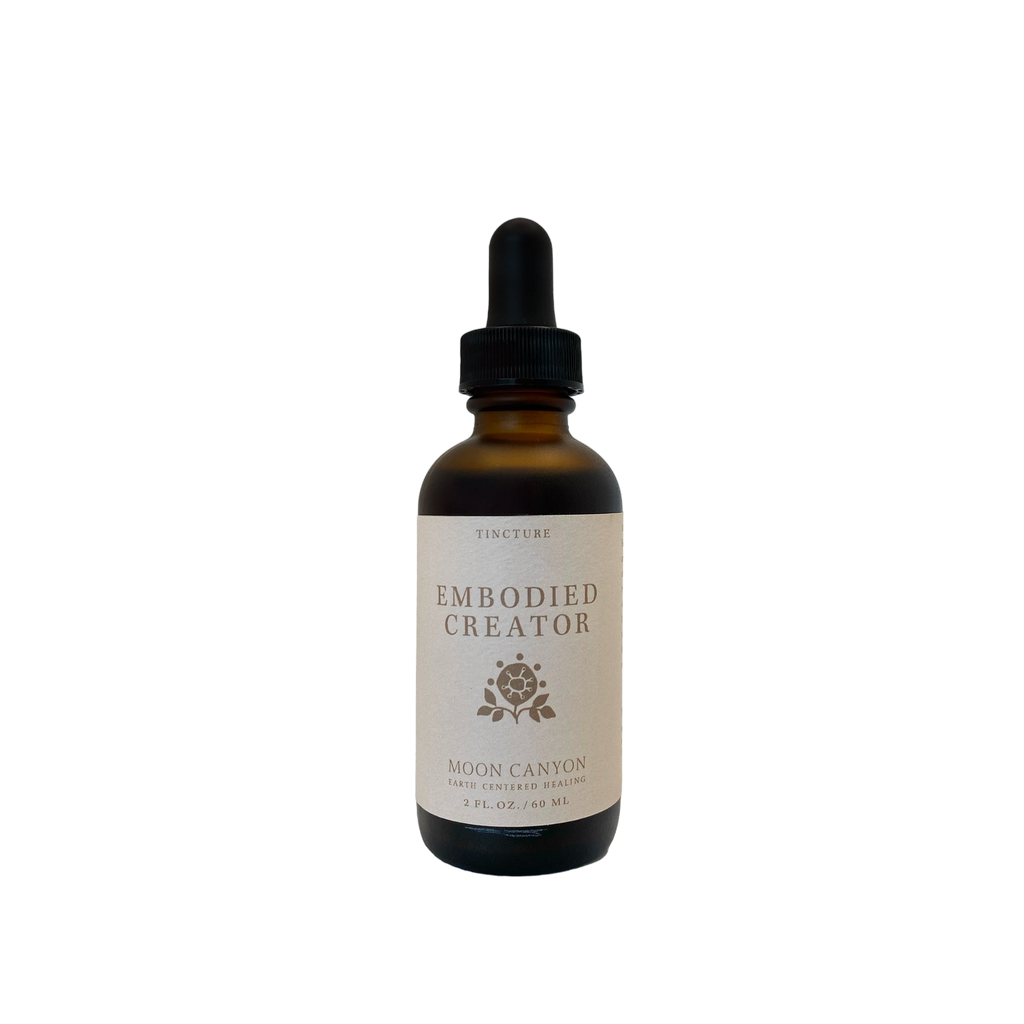 The Embodied Creator Tincture from Moon Canyon Healing comes in a brown glass bottle with a black dropper cap. The label, which features a minimalist design with a small rose icon and specifies the product as a tincture measuring 2 fl. oz. (59 mL), stands out against the black background.