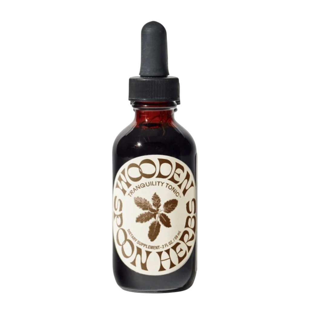 A brown glass dropper bottle labeled "Tranquility Tonic" by WOODEN SPOON HERBS, featuring a plant graphic, black dropper cap, and crafted with organic herbs for natural stress relief.