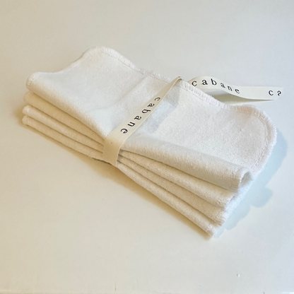 A set of four ORGANIC WASHCLOTHS by cabane childrenswear, handmade in Vancouver from organic cotton, is neatly folded and tied with a white ribbon reading "cabane," displayed on a plain white surface.