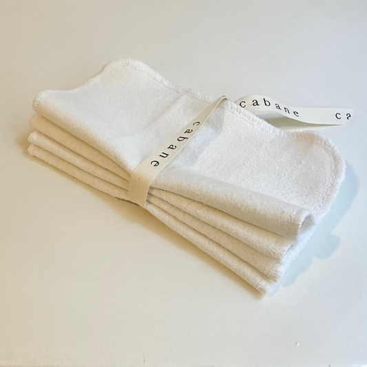 A set of four ORGANIC WASHCLOTHS by cabane childrenswear, handmade in Vancouver from organic cotton, is neatly folded and tied with a white ribbon reading "cabane," displayed on a plain white surface.